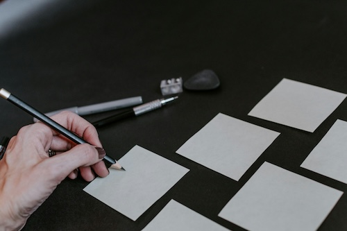 hand holding a pencil over a post it
